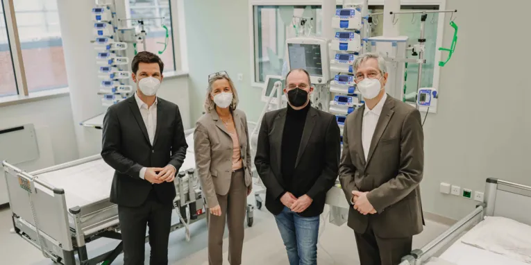 Vier Personen in einem Krankenhauszimmer mit vielen Überwachungsgeräten